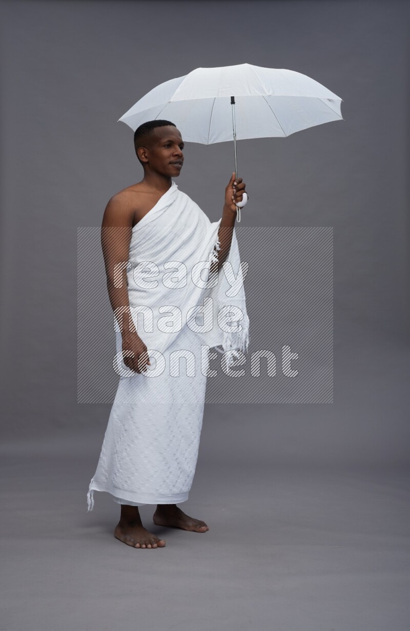 A man wearing Ehram Standing holding umbrella on gray background