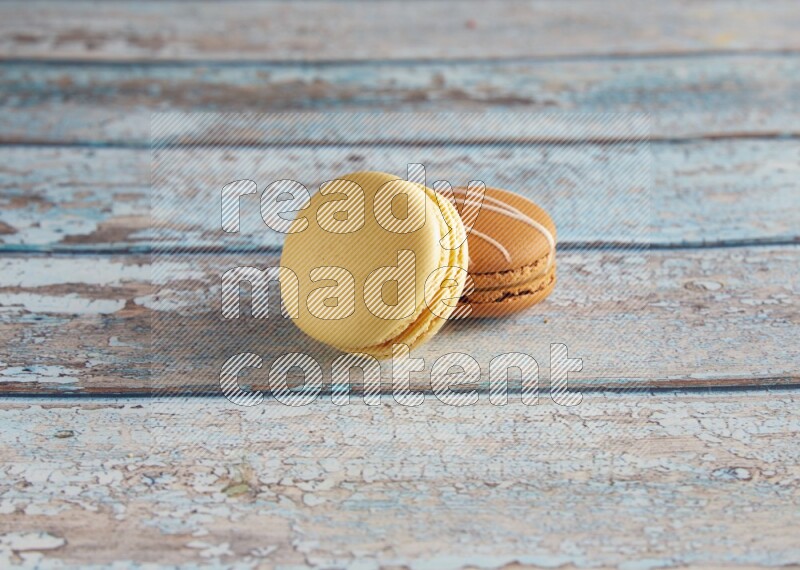 45º Shot of of two assorted Brown Irish Cream, and Yellow Vanilla macarons on light blue background