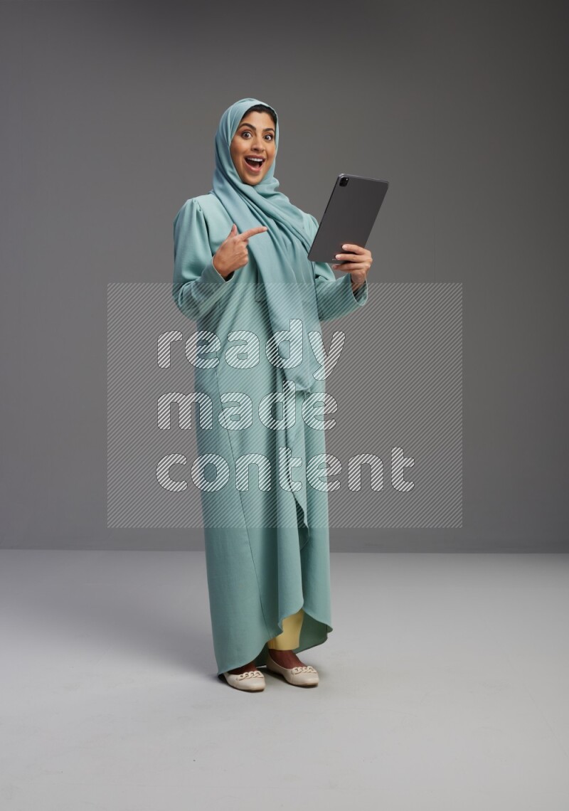 Saudi Woman wearing Abaya standing working on tablet on Gray background