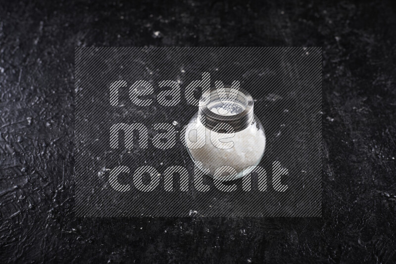 وعاء زجاجي ممتلئ بملح البحر الخشن على خلفية سوداء