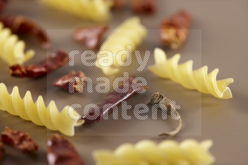 Raw pasta with different ingredients such as cherry tomatoes, garlic, onions, red chilis, black pepper, white pepper, bay laurel leaves, rosemary and cardamom on beige background
