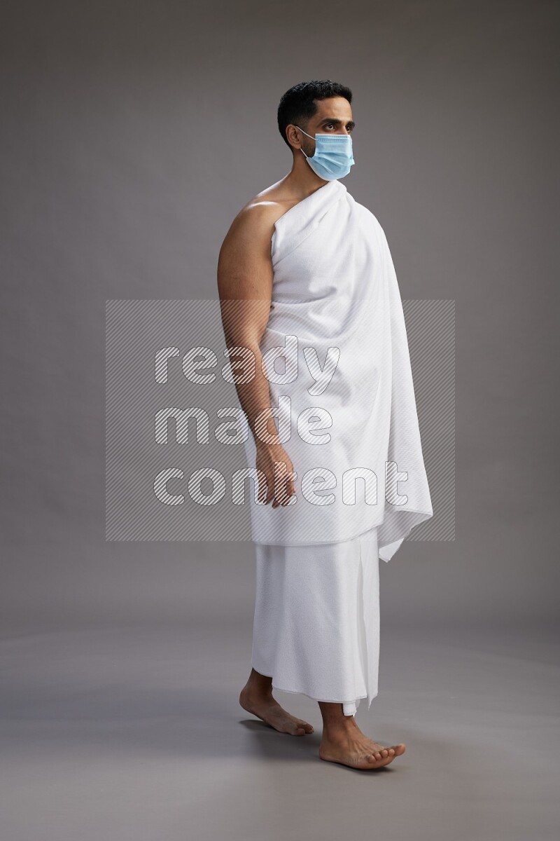 A man wearing Ehram with face mask Standing Interacting with the camera on gray background