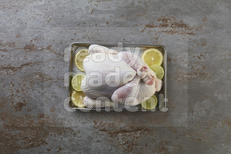 whole Raw chicken on a small oven trey direct on a rustic grey background