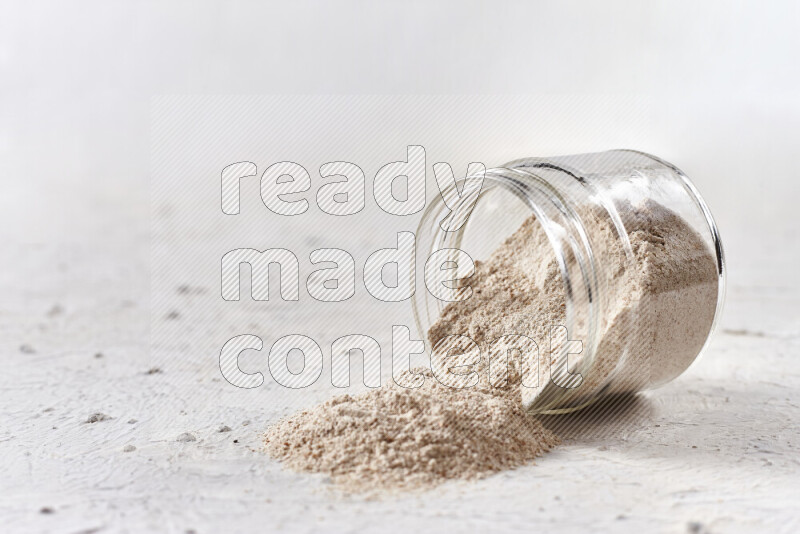 A glass jar full of onion powder flipped with some spilling powder on white background
