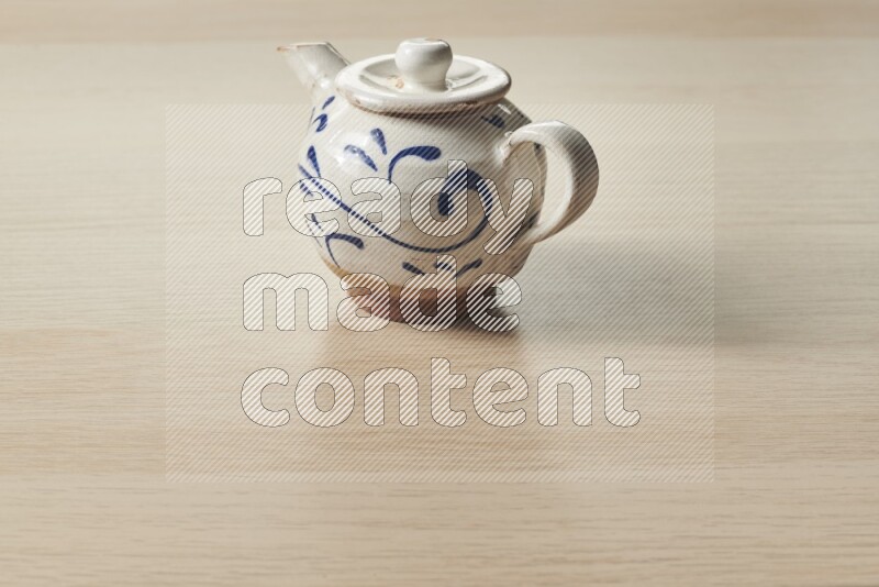 A pottery teapot on light wooden background