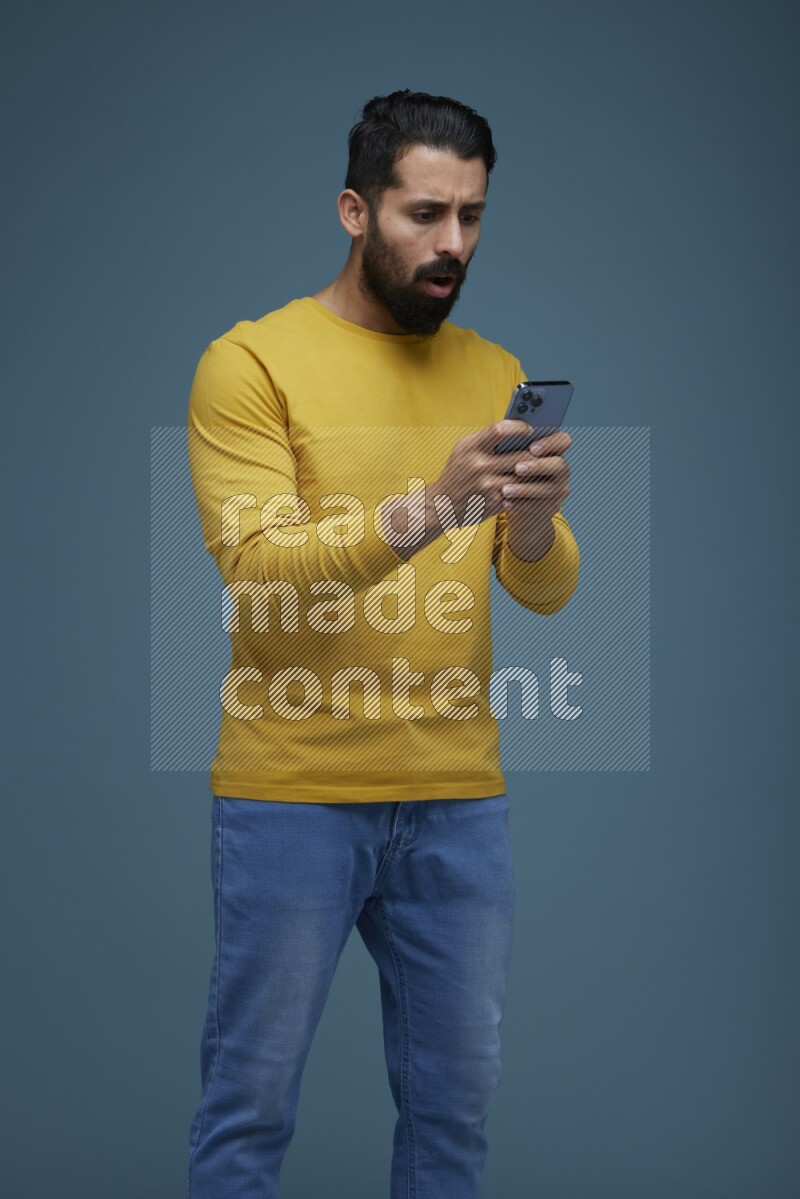 Man typing on his phone in a blue background wearing a yellow shirt