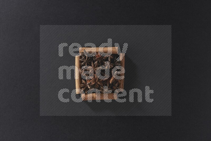 أربعة من أعواد القرفة مكونة شكل مربع بداخلها يانسون نجمي علي خلفية سوداء