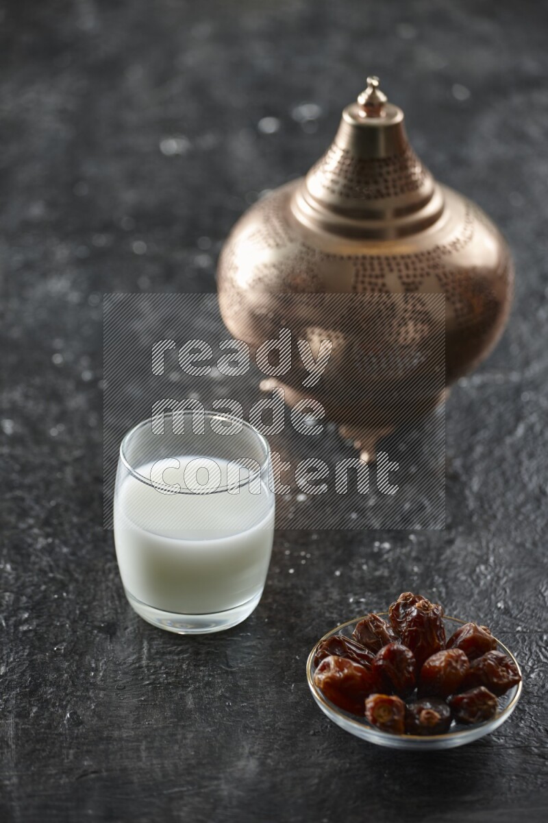 A golden lantern with different drinks, dates, nuts, prayer beads and quran on textured black background