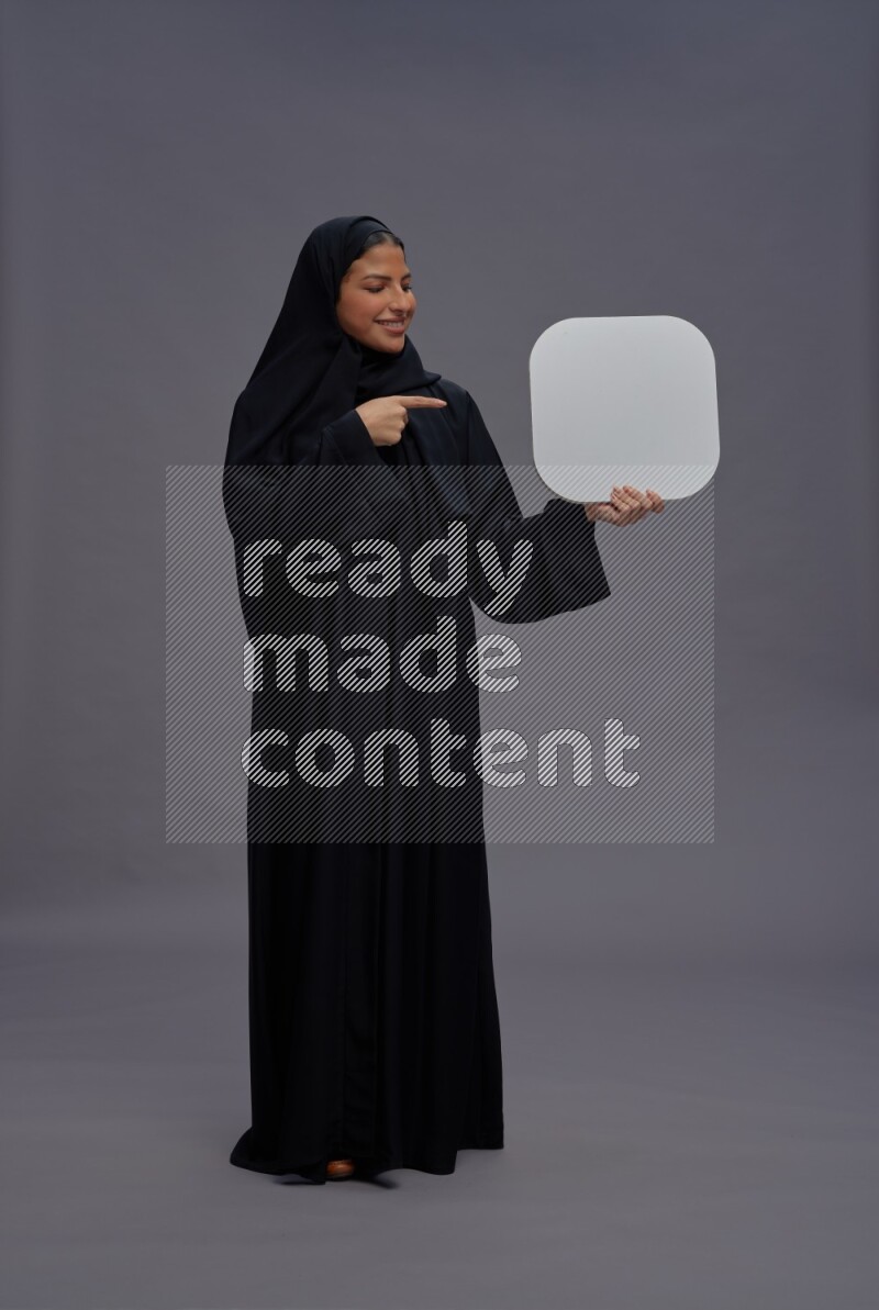 Saudi woman wearing Abaya standing holding social media sign on gray background