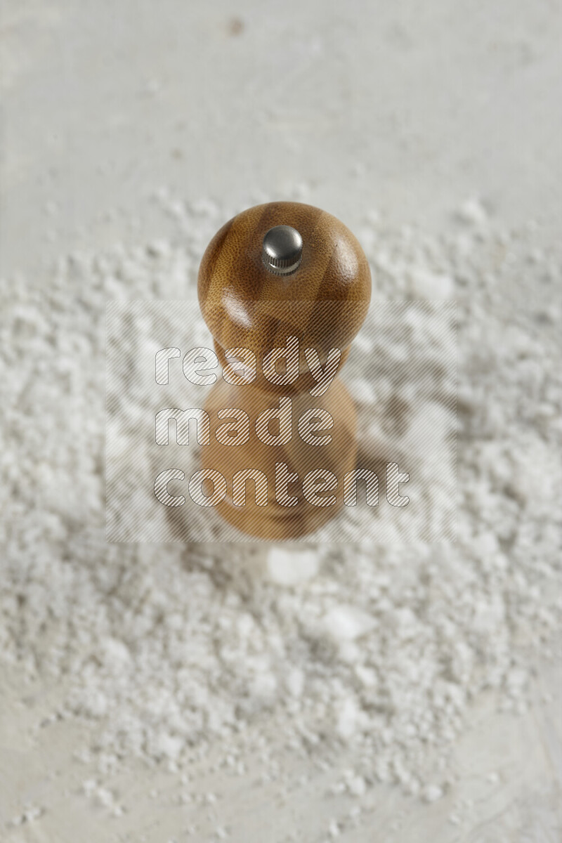 A wooden grinder standing upright and surrounded by coarse white seaa salt on white background
