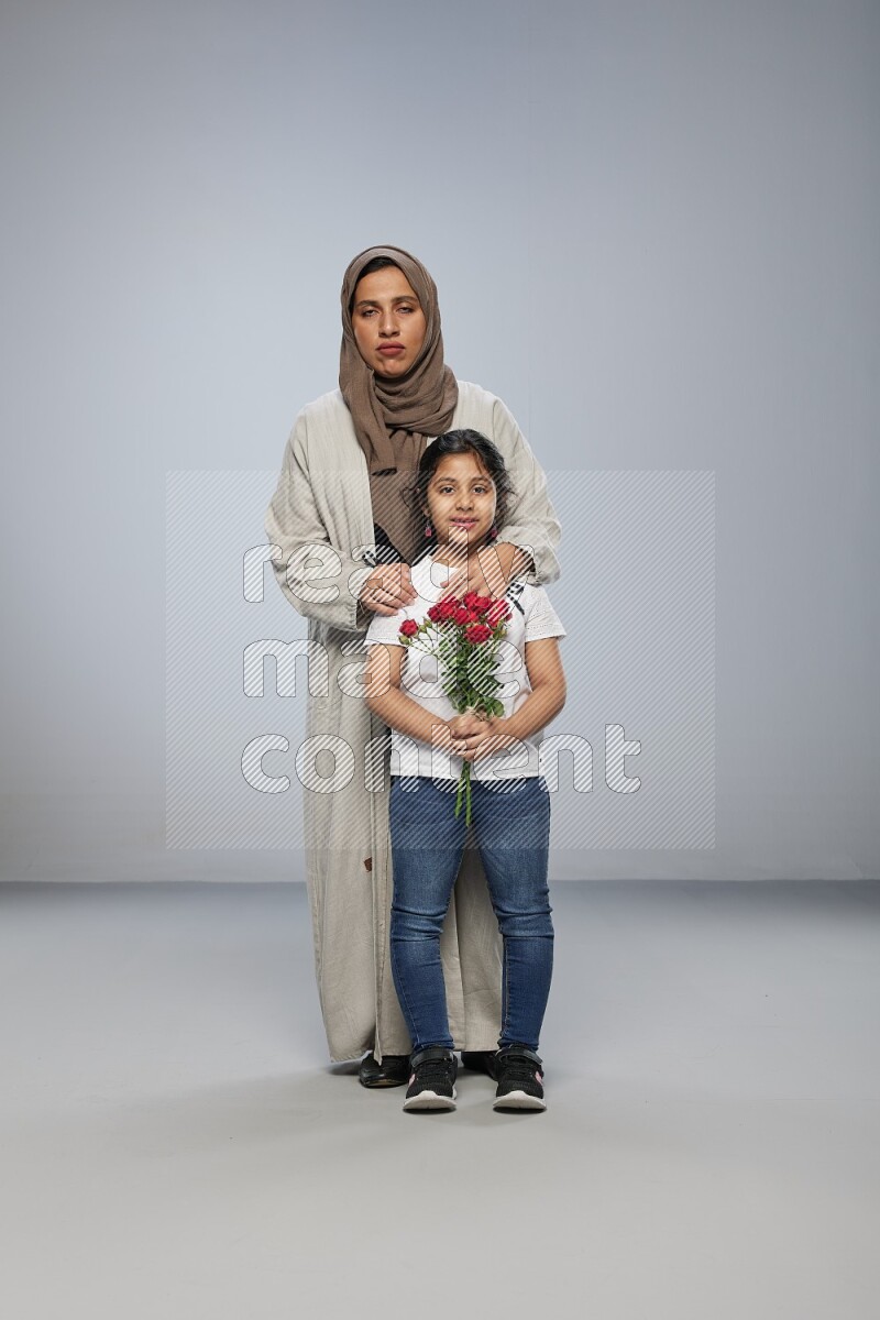 A girl standing giving flowers to her mother on gray background