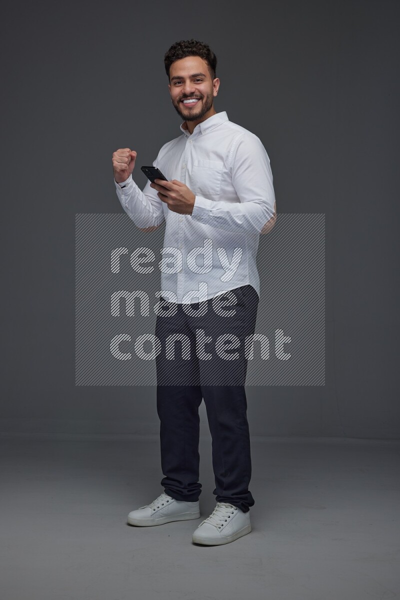 A man wearing smart casual standing and using his phone eye level on a gray background
