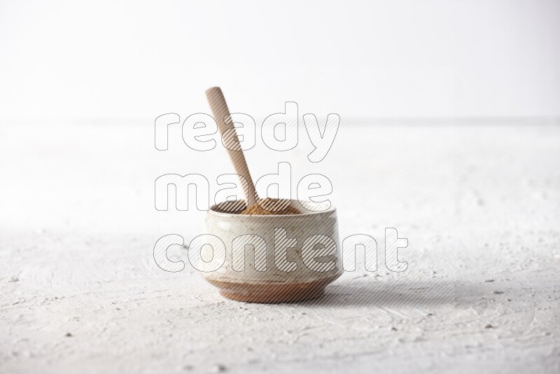 Ceramic beige bowl full of cinnamon powder with a wooden spoon on a textured white background