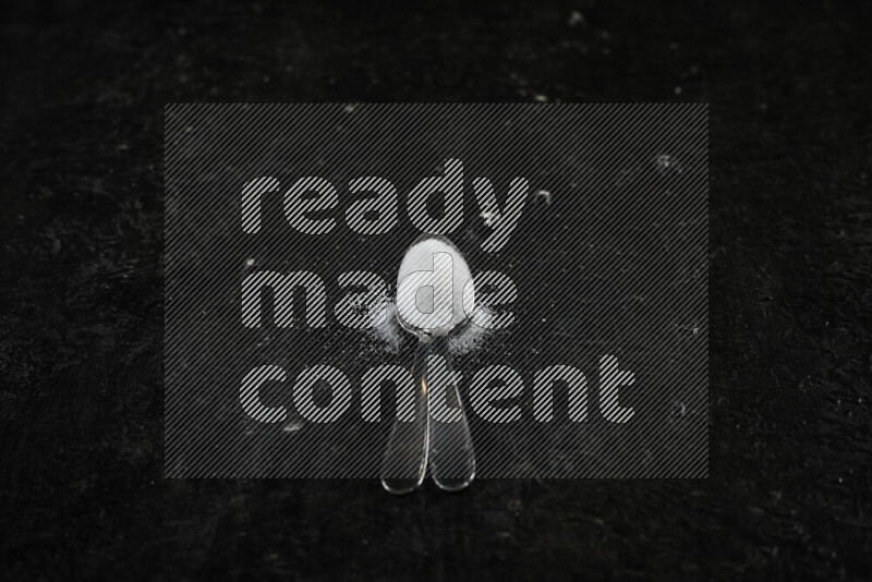 2 metal spoons filled with white salt on black background