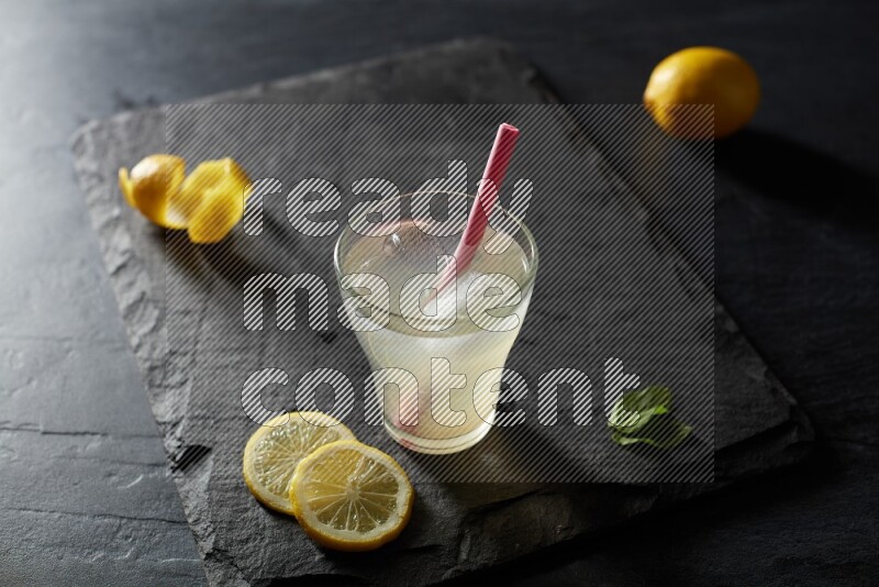 A glass of lemon juice with a straw on black background