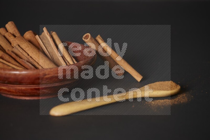 Cinnamon sticks in wooden bowl and cinnamon powder in a wooden spoon on black background