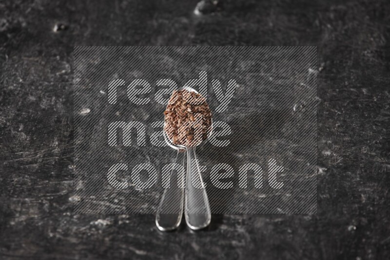 ملعقتان معدنيتان ممتلئتان بحبوب بذر الكتان علي خلفية سوداء