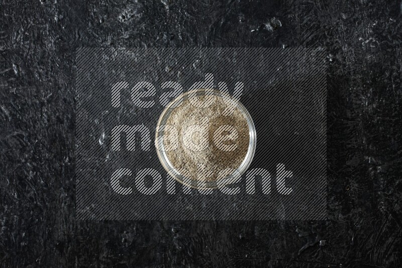 A glass bowl full of cardamom powder on textured black flooring