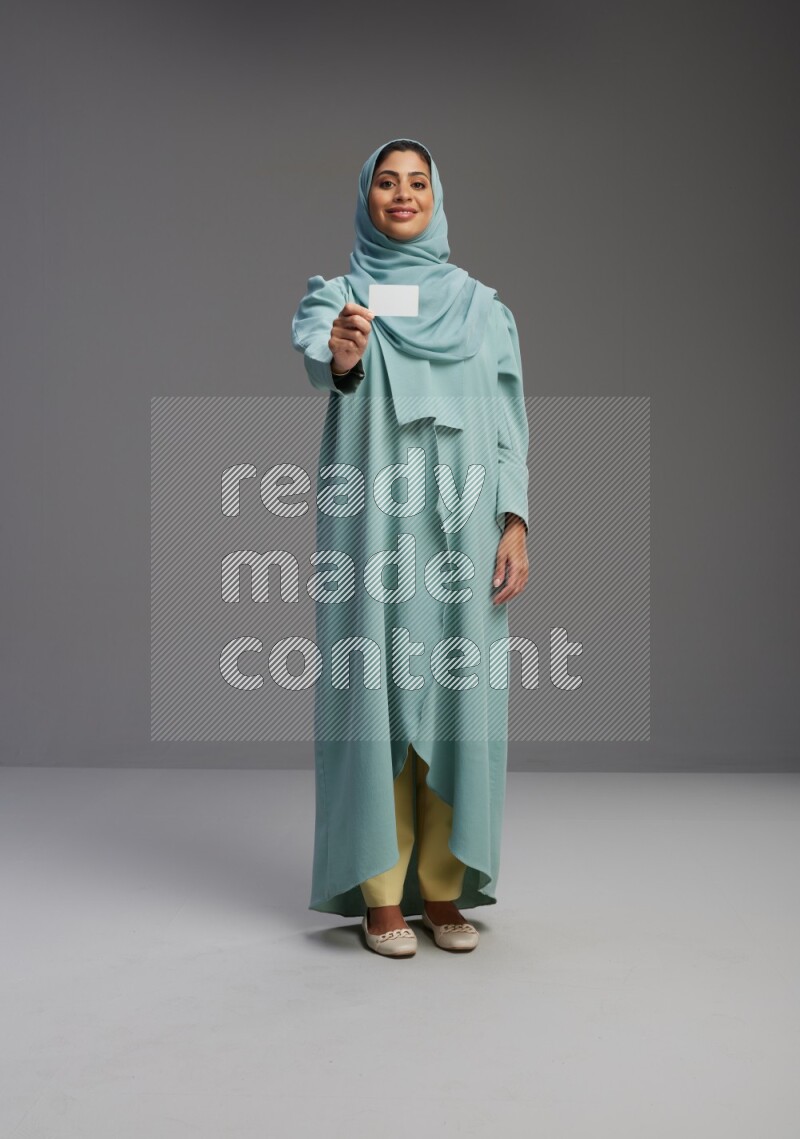 Saudi Woman wearing Abaya standing holding ATM card on Gray background