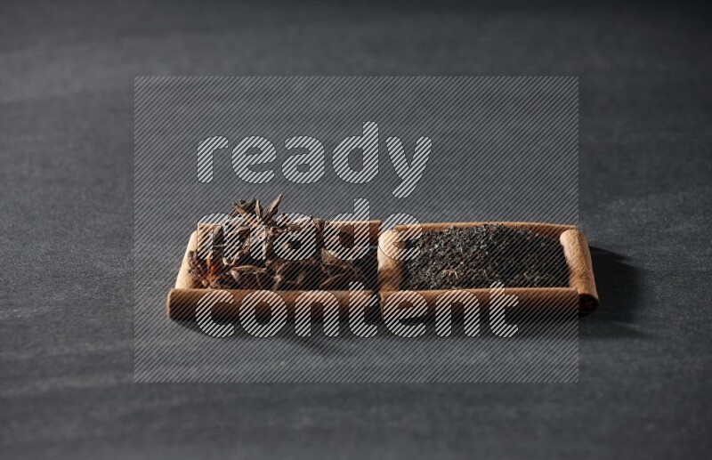 مربعان من أعواد القرفة ممتلئان باليانسون النجمي والشاي الأسود علي خلفية سوداء