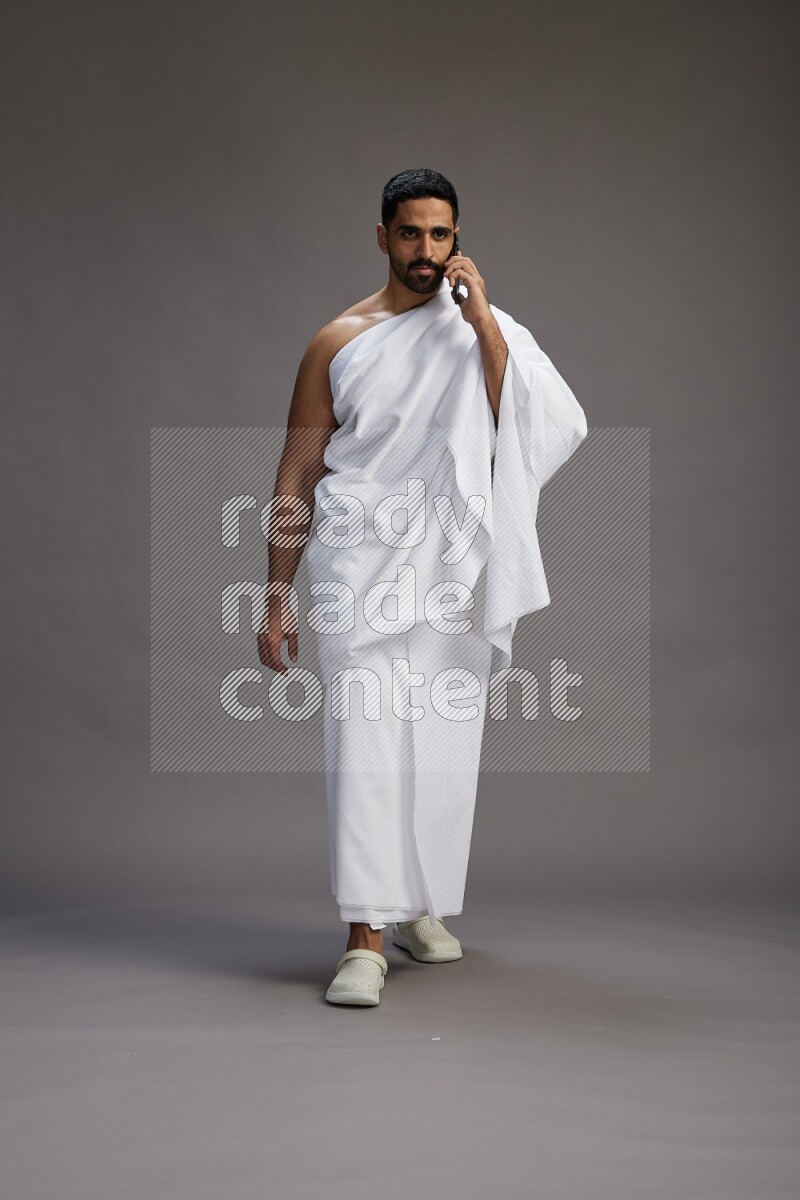 A man wearing Ehram Standing talking on phone on gray background