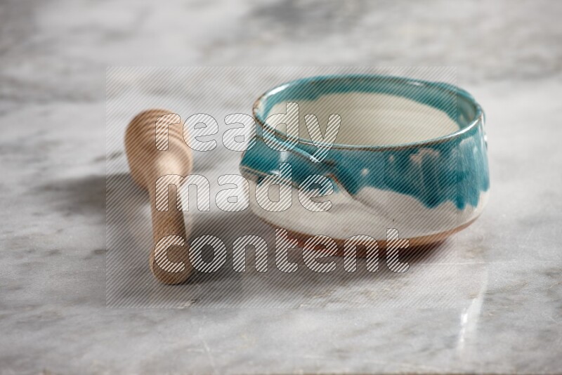 Multicolored pottery bowl with wooden honey dipper on the side on grey marble background