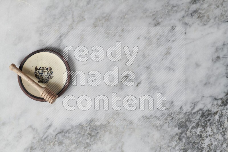 طبق فخاري مزخرف مع ملعقة عسل خشبية بداخله على خلفية من الرخام الرمادي