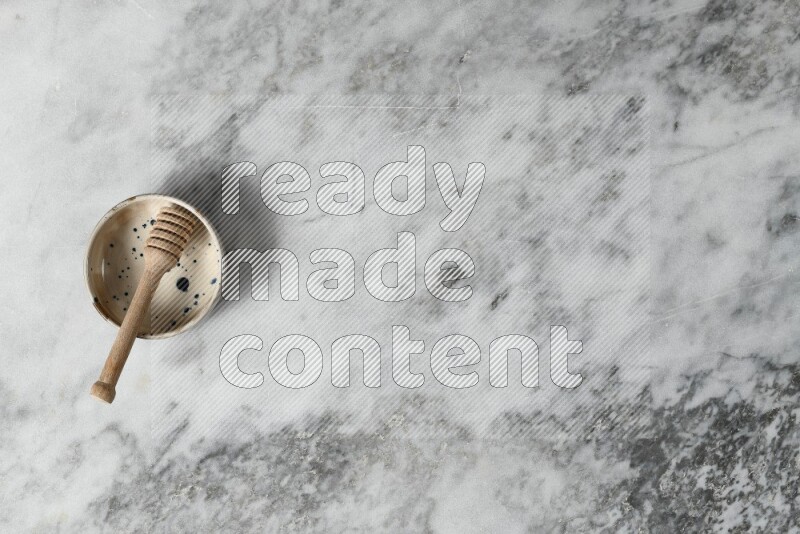 وعاء فخاري متعدد الألوان مع ملعقة عسل خشبية بداخله على خلفية من الرخام الرمادي