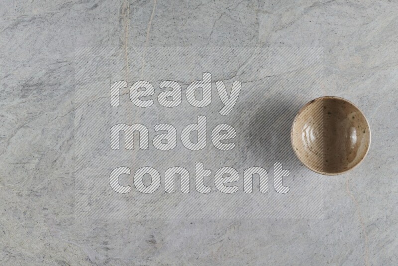 A small beige pottery bowl on grey marble background