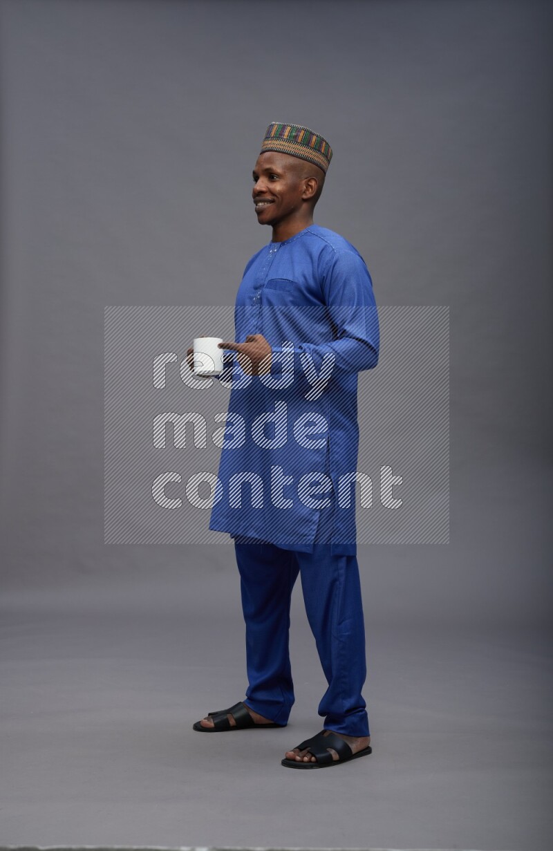 Man wearing Nigerian outfit standing holding mug on gray background