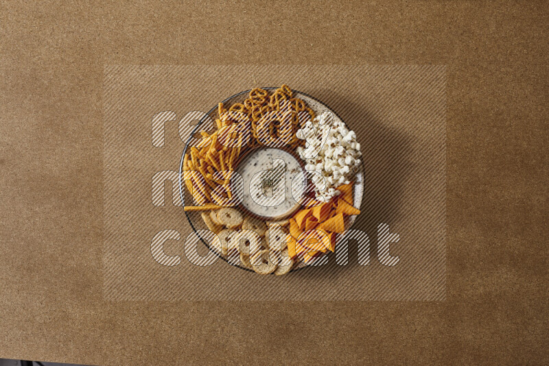 Assorted snacks on a pottery plate with a dipping on brown background