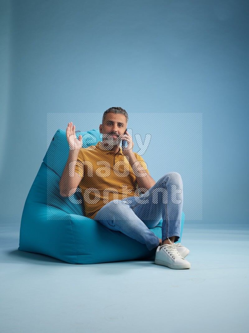 A man sitting on a blue beanbag and talking on the phone