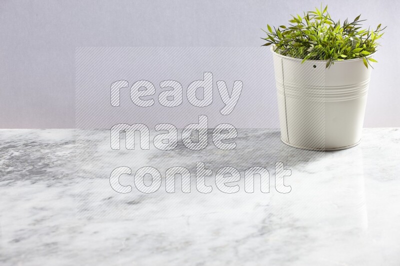 Green artificial plant in white pot on light grey marble background