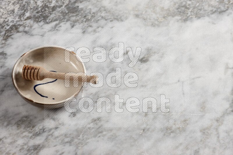 Multicolored pottery bowl with wooden honey dipper in it on grey marble background