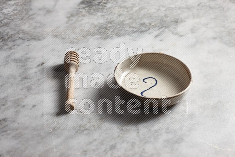 Multicolored pottery bowl with wooden honey dipper on the side on grey marble background