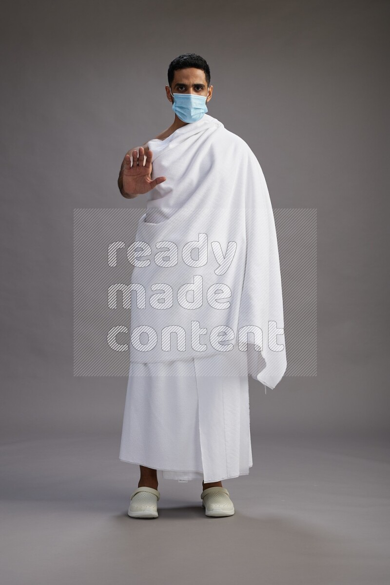A man wearing Ehram with face mask Standing Interacting with the camera on gray background
