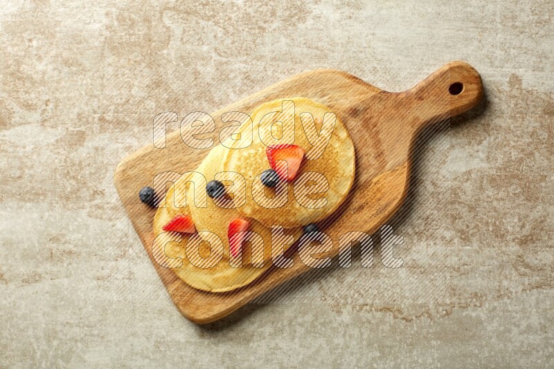 Three stacked mixed berries pancakes on a wooden board on beige background