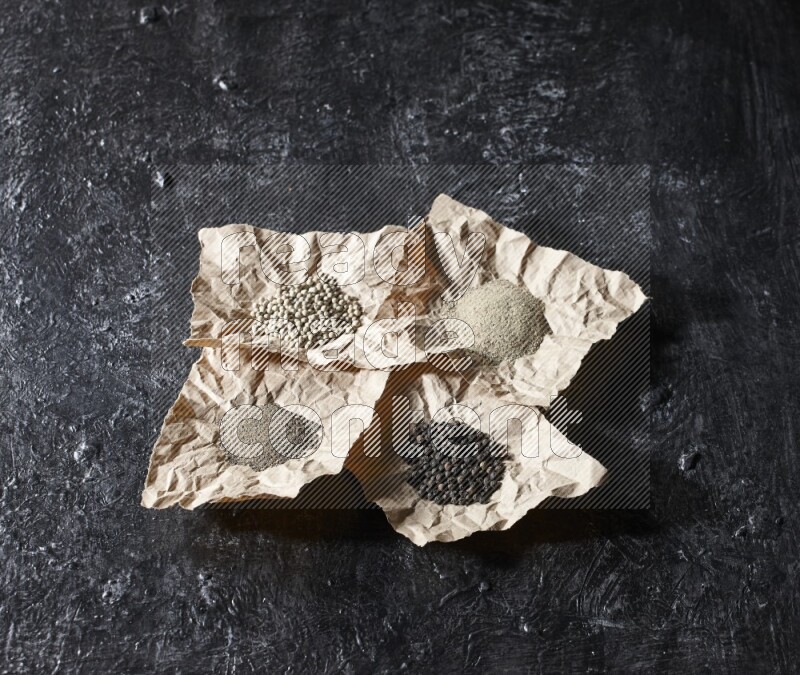 Crumpled pieces of paper full of black and white pepper beads and powder on a textured black flooring