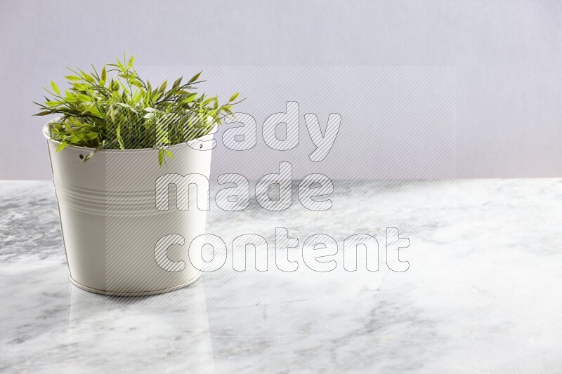 Green artificial plant in white pot on light grey marble background