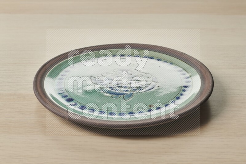 A decorative pottery plate on light wooden background