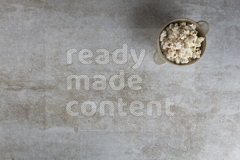 popcorn in a off-white handheld ceramic bowl on a grey textured countertop