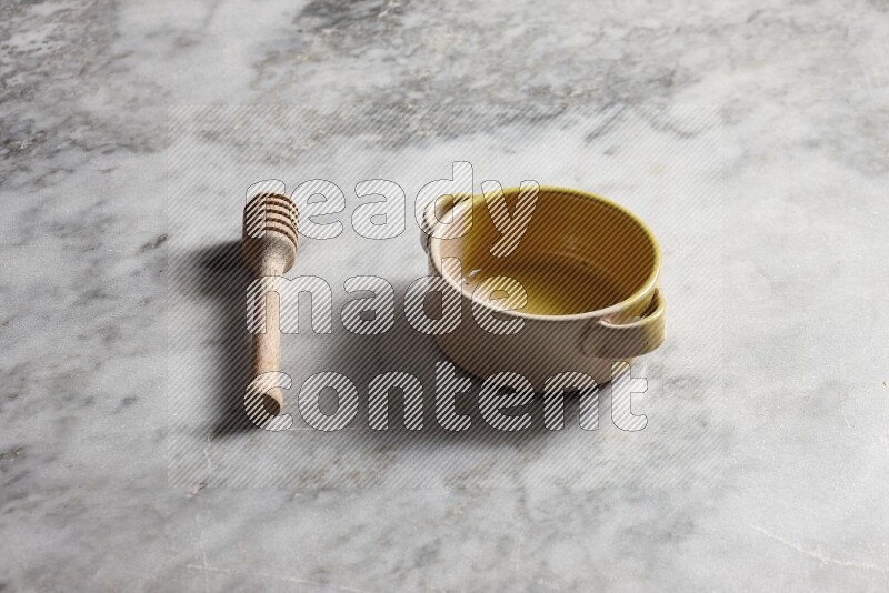 Multicolored pottery bowl with wooden honey dipper on the side on grey marble background