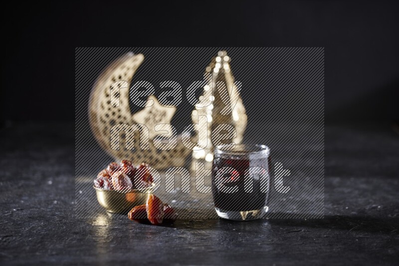 Dates in a metal bowl and tamarand beside a gold crescent and a lantern in a dark setup