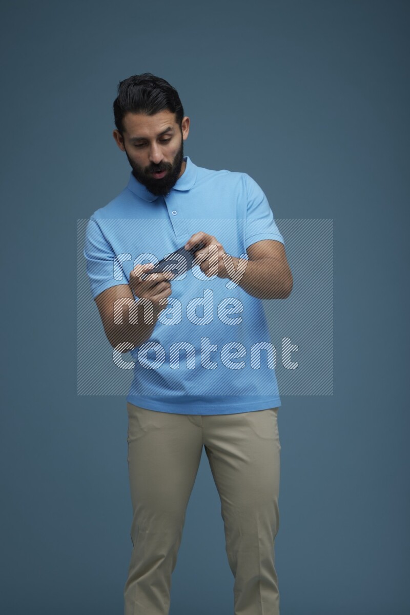 Man playing a game on his phone in a blue background wearing a Blue shirt