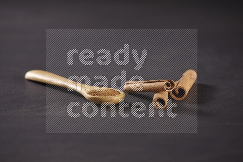3 Cinnamon sticks stacked beside a wooden spoon full of cinnamon powder on black background in different angles