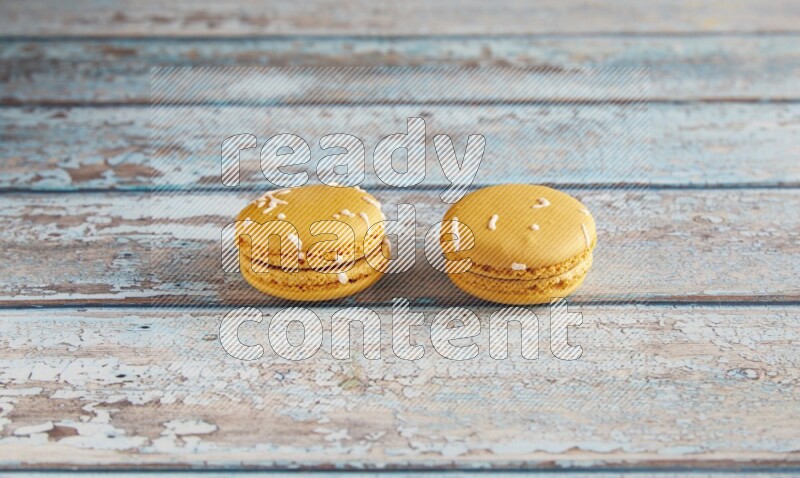 45º Shot of two Yellow Piña Colada macarons on light blue wooden background