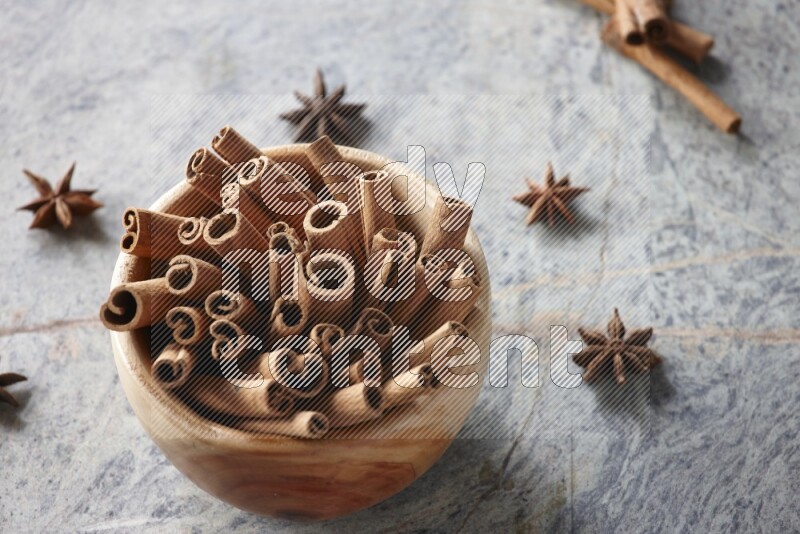 wooden bowl full of cinnamon sticks surrounded by star anis on marble background in different angles
