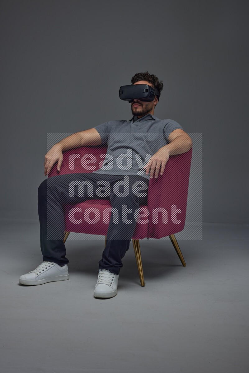A man wearing casual and wearing VR while sitting on a burgundy chair eye level on a gray background