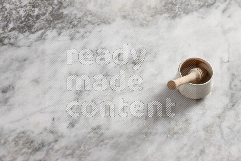 Beige pottery bowl with wooden honey dipper in it on grey marble background