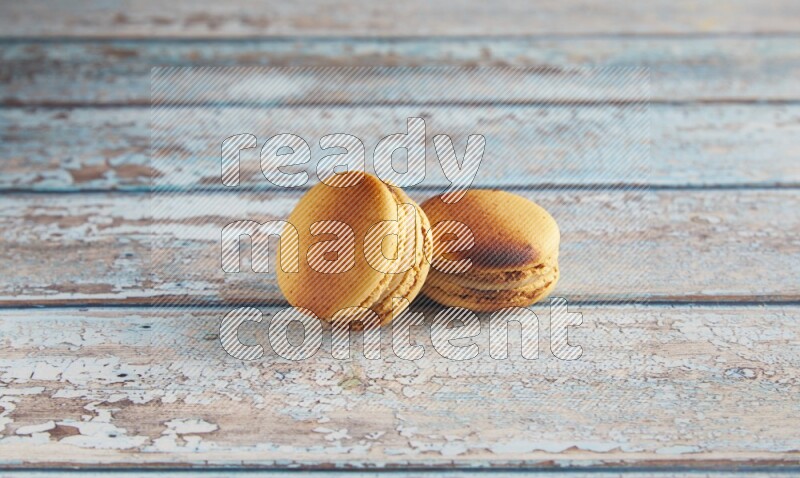 45º Shot of two Yellow Crème Brulée macarons on light blue wooden background